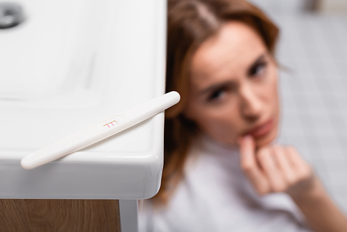 pregnancy test with positive result near worried woman on blurred background