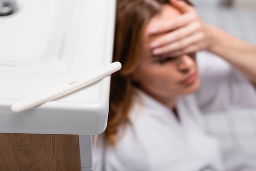 pregnancy test with positive result near worried woman on blurred background in bathroom