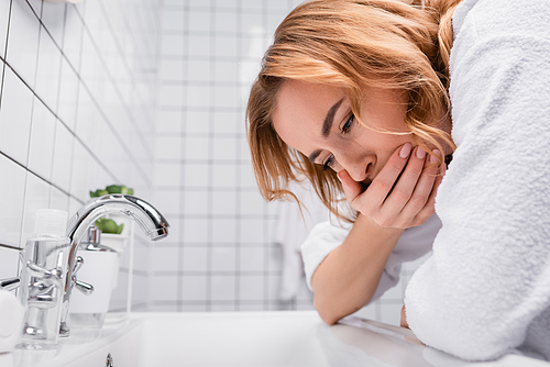 pregnant woman covering mouth while feeling nausea near sink in bathroom