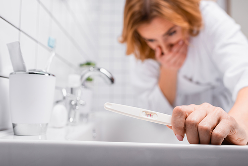 pregnancy test in hand on pregnant woman in bathrobe feeling nausea on blurred background