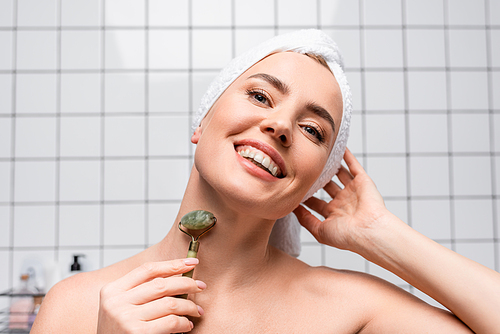 cheerful woman with towel on head using jade roller in bathroom