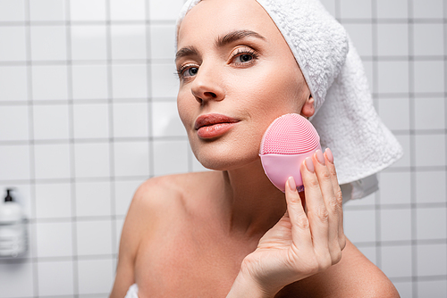 woman in towel on head using cleansing silicone brush in bathroom