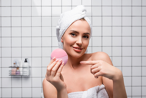 joyful woman in towel on head pointing with finger at silicone brush in bathroom