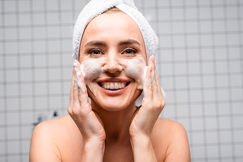 happy woman with naked shoulders applying foam cleanser in bathroom