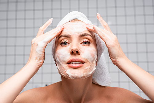 woman with naked shoulders applying foam cleanser in bathroom