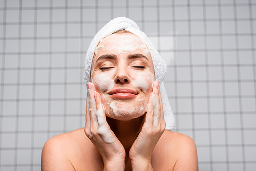 happy woman with closed eyes applying foam cleanser in bathroom