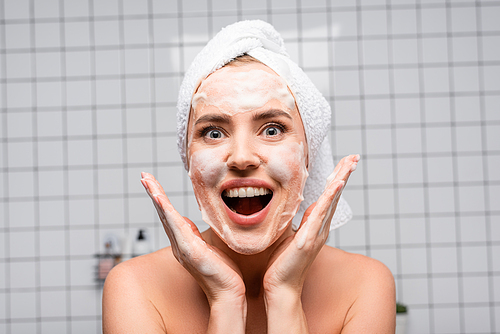 amazed woman with naked shoulders applying foam cleanser in bathroom