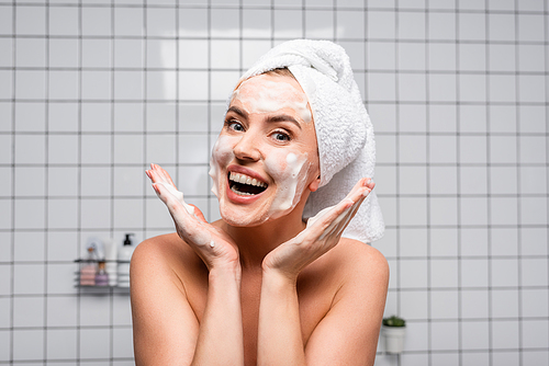 excited woman with naked shoulders applying foam cleanser in bathroom