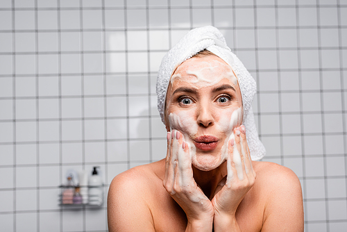 surprised woman with naked shoulders applying foam cleanser in bathroom