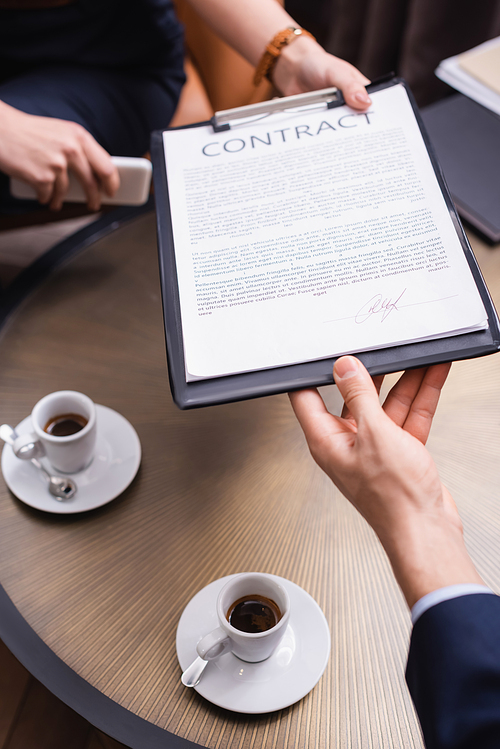 Cropped view of businessman taking contract from businesswoman near coffee in restaurant