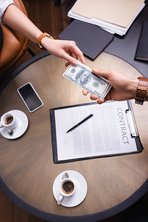 Cropped view of business people holding dollars near contract and coffee in restaurant