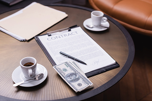 Dollars near cup of coffee and contract on blurred background in restaurant