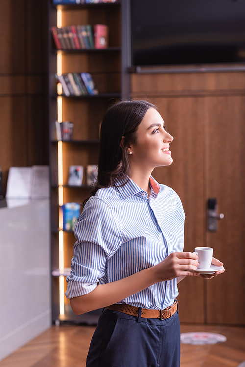 smiling businesswoman holding cup of coffee and looking away in restaurant