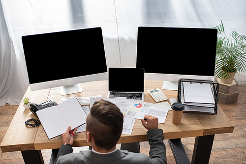 overhead view of trader holding empty notebook near monitors with blank screen