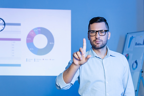 businessman in glasses pointing with finger near charts and graphs