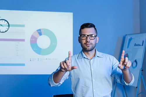 businessman in glasses pointing with fingers near charts and graphs