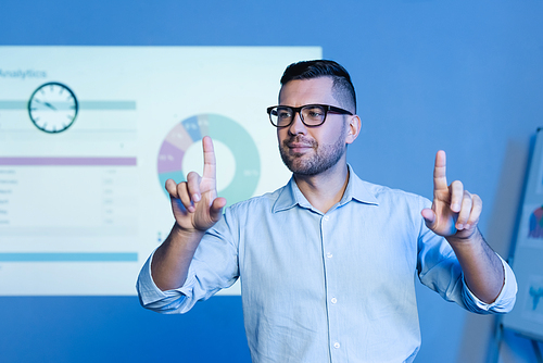 businessman in glasses pointing with fingers near charts and graphs on wall