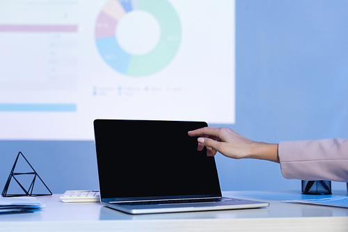 cropped view of businesswoman pointing with finger at laptop with blank screen on desk
