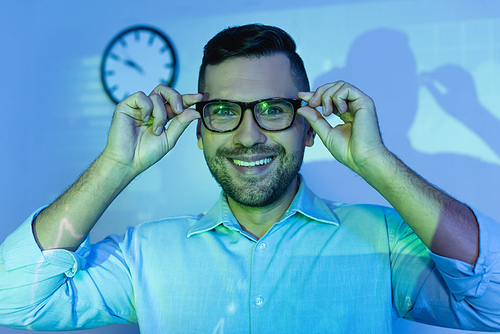 happy businessman adjusting glasses and smiling in office