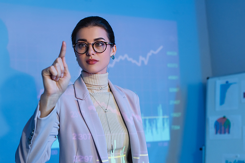businesswoman in suit and glasses and pointing with finger near digital graphs
