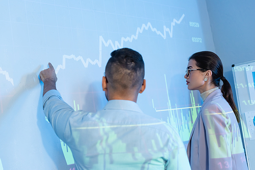 businessman pointing with finger at wall with digital graphs near colleague