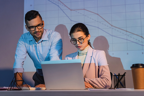 business people in glasses looking at laptop with digital charts on wall on background