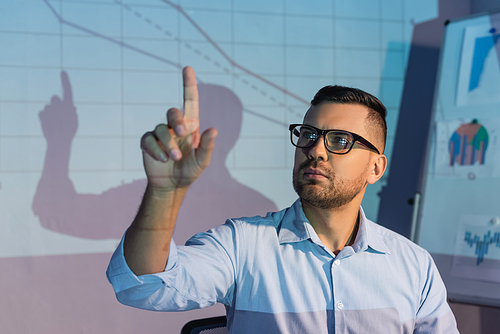 businessman in glasses while pointing with finger near digital graphs