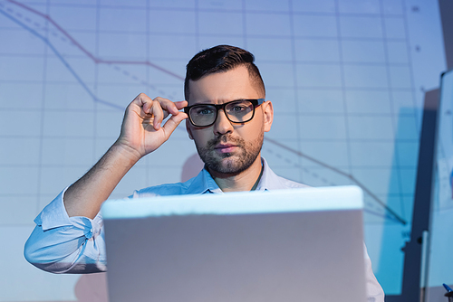 businessman adjusting glasses while looking at laptop