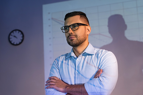 businessman in glasses standing with crossed arms in office