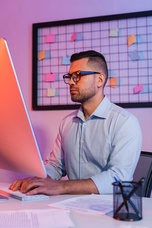 businessman in glasses typing on computer keyboard and looking at monitor