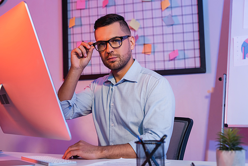 businessman adjusting glasses near computer keyboard and monitor