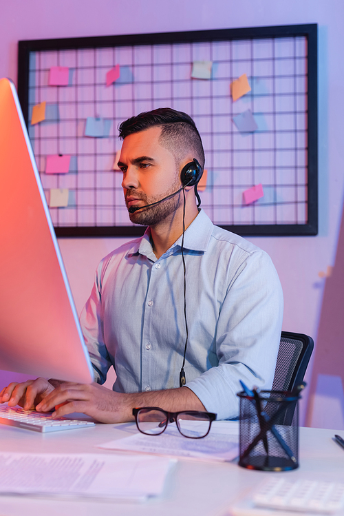 operator in headset typing on computer keyboard and looking at monitor