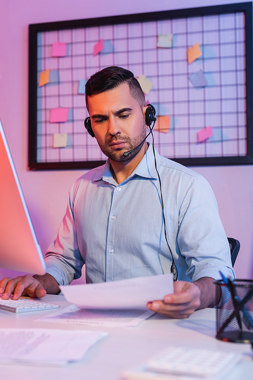 operator in headset looking at paper near computer monitor