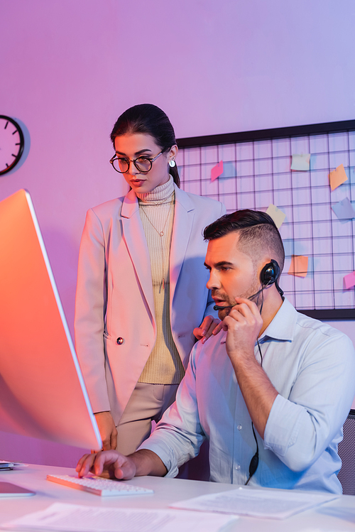 operator in headset looking at computer monitor near businesswoman