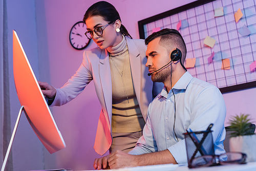 operator in headset looking at computer monitor near businesswoman in office