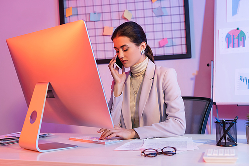 businesswoman talking on smartphone and looking at computer keyboard in office