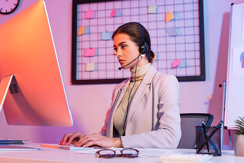 female operator in headset typing on computer keyboard and looking at monitor