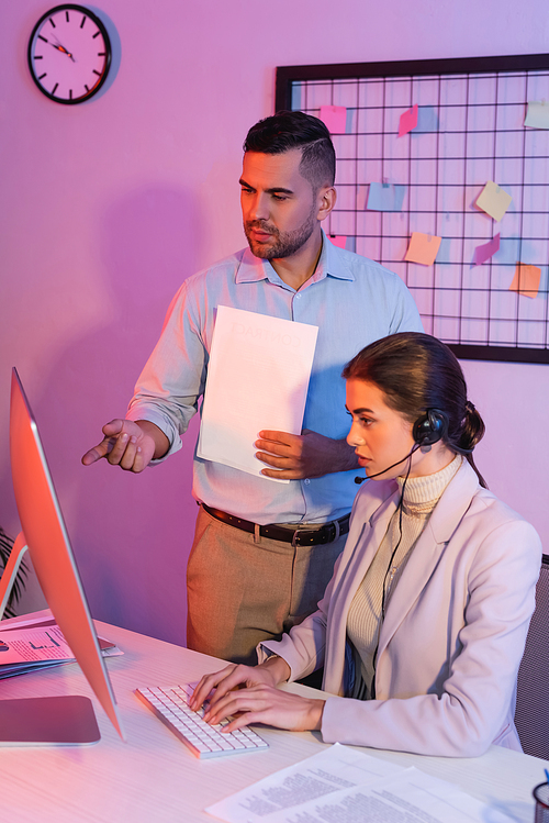 businessman pointing with finger at computer monitor near female operator in headset