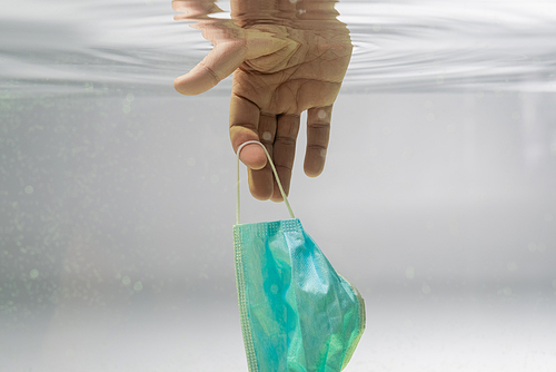 partial view of male hand with used protective mask in water, ecology concept