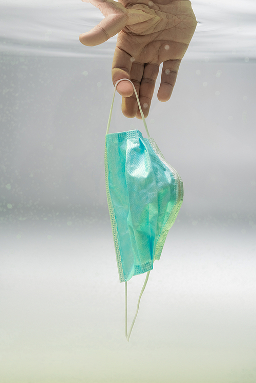 cropped view of male hand with medical mask in water, ecology concept