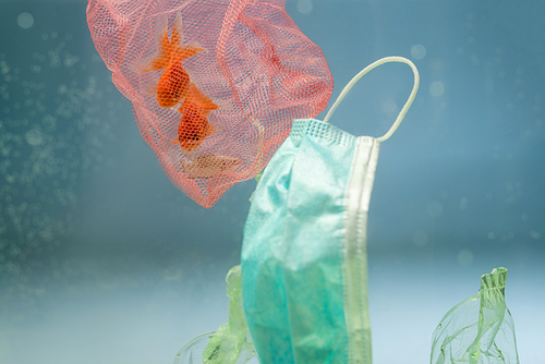 net with goldfishes near medical mask and cellophane rubbish in water, ecology concept