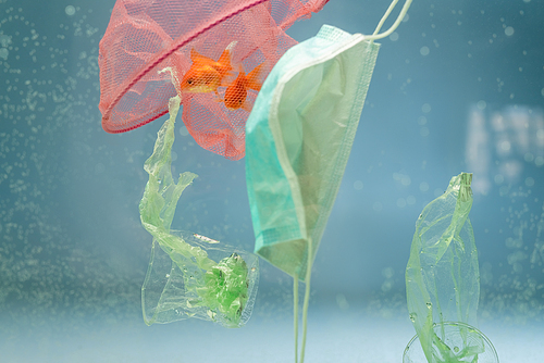 net with goldfishes, medical mask, plastic bags and cups in water, ecology concept