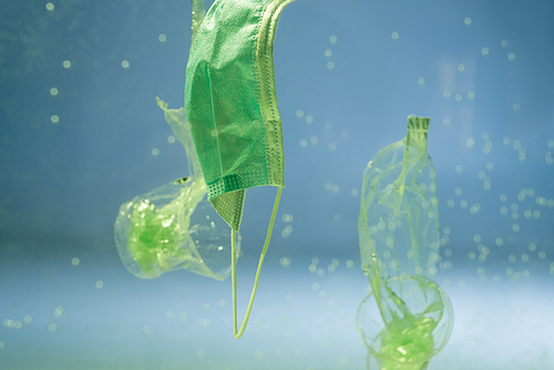 plastic bags and cups near used medical mask in water, ecology concept