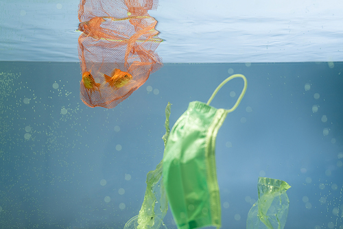 protective mask near net with goldfishes in water, ecology concept