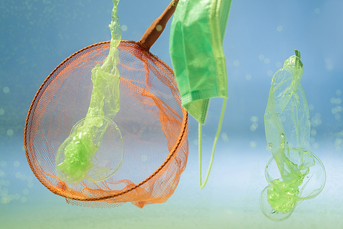 scoop-net near medical mask and plastic bags in water, ecology concept