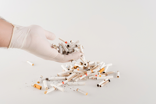 cropped view of male hand in latex glove near cigarette ends on white, ecology concept