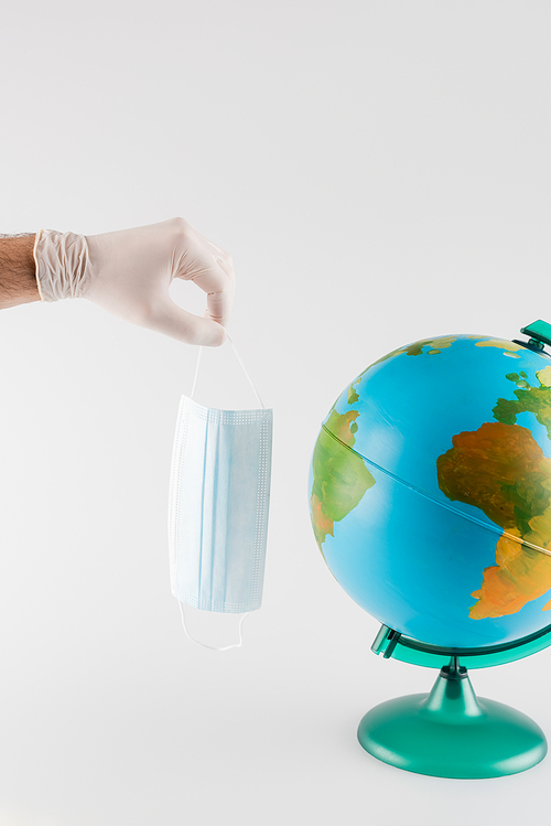 globe near man in latex glove holding medical mask isolated on grey, cropped view, ecology concept