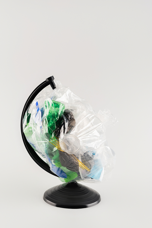 cellophane pack with plastic garbage on globe stand isolated on grey, ecology concept