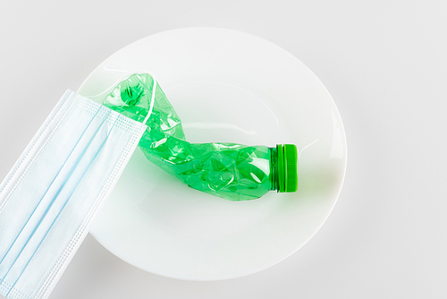 top view of medical mask and crumpled plastic bottle on white, ecology concept