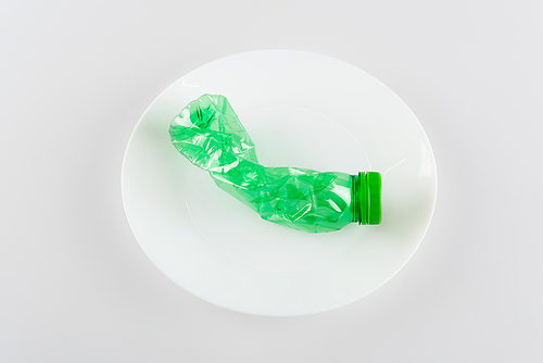 top view of plate with used plastic bottle on white, ecology concept